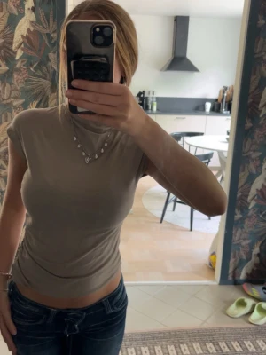Beige polotopp med kort ärm - Snygg beige polotopp med korta ärmar och figurnära passform. Perfekt att styla med jeans eller kjol för en trendig look. Mjuk och stretchig i materialet för extra komfort.