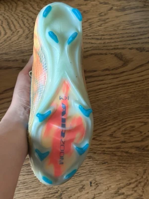 Nike Air Zoom Mercurial fotbollsskor storlek 39 - Säljer ett par Nike Air Zoom Mercurial fotbollsskor med guldfärgad ovandel och blå detaljer. Skorna har genomskinlig sula med blå dobbar och orange inslag. Tillverkade i syntetmaterial med snörning och låg vikt för maxad speed på planen.