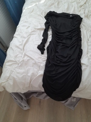Svart långärmad omlottklänning - Svart långklänning med långa ärmar och omlottdetaljer. Klänningen har rynkade partier längs sidorna som ger en snygg siluett. Perfekt för dig som gillar en elegant och stilren look.