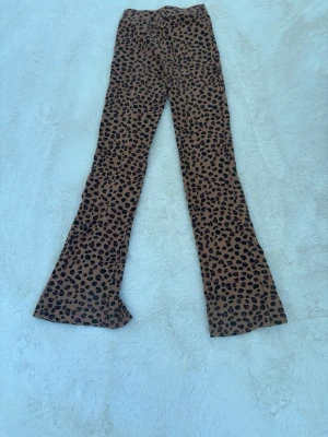 Bruna leopardmönstrade leggings - Snygga bruna leggings med leopardmönster och utsvängda ben. De har en hög midja och slitsar längst ner på benen. Perfekta för dig som vill sticka ut med ett djurmönster. Materialet är stretchigt och bekvämt.