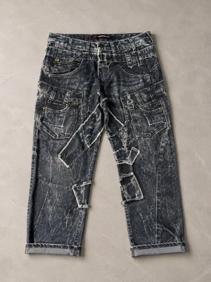  Cipo & BAXX Jeans mörkblå  - Cipo & Baxx mörkblåa jeans, storlek W:30 L:32 med en unik design som inkluderar flera fickor och dekorativa sömmar. Byxorna har en mörk tvätt med ljusare partier som ger en sliten look. Detaljer som synliga sömmar och tygapplikationer bidrar till en distinkt stil. Midjan har bälteshällor och knäppning med dragkedja och knapp.