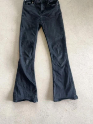 Svarta bootcut jeans - Säljer ett par svarta bootcut jeans med hög midja och klassiska fem fickor. Jeansen har utsvängda ben och är tillverkade i ett mjukt denimtyg. Perfekta för dig som gillar en retroinspirerad look.