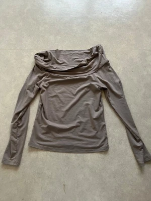 Beige offshoulder topp - Snygg beige offshoulder topp med långa ärmar och bred krage. Tillverkad i mjukt material som sitter skönt mot kroppen. Perfekt för dig som vill ha en stilren och trendig look.