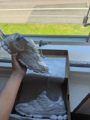 Asics gel nyc cream cloud grey 43,5 - Snygga vita ASICS sneakers med en chunky sula och detaljer i mesh och syntetläder. Skorna har klassisk snörning och diskret logga på sidan. Perfekta för dig som gillar stilrena och sportiga sneakers med modern vibe.