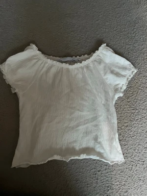 Vit kortärmad blus med volangkant - Tryck gärna köp nu🩷🩷 Söt vit blus med korta ärmar och volangkant vid halsringning och ärmslut. Tillverkad i ett lätt, krinklat material som ger en avslappnad och trendig look. Perfekt att matcha med jeans eller kjol för en fräsch stil.