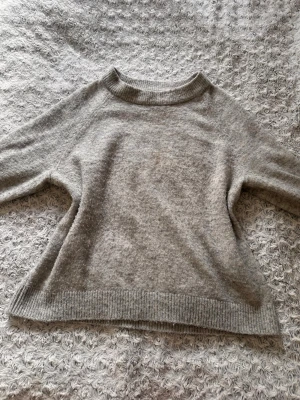 Grå stickad tröja från Vero Moda - Mysig grå stickad tröja från Vero Moda med rund halsringning och ribbade muddar vid ärmslut och nederkant. Den är perfekt till jeans eller kjol en svalare sommardag m.m. Tröjan är lite nopprig men fortfarande mycket fin!