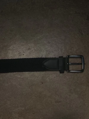 Mörkblått flätat bälte med metallspänne - Stilrent mörkblått flätat bälte med klassiskt silverfärgat metallspänne. Bältet har en enkel och tidlös design som passar till de flesta outfits. Perfekt accessoar för att lyfta din look. Hör gärna av dig vid intresse! 