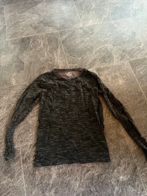 Mörkgrå långärmad topp - En stilren mörkgrå långärmad topp med diskret mönster. Toppen har rund halsringning och är tillverkad i ett mjukt material som känns bekvämt mot huden. Perfekt att matcha med jeans eller kjol för en enkel och snygg look. (Plus frakt) 