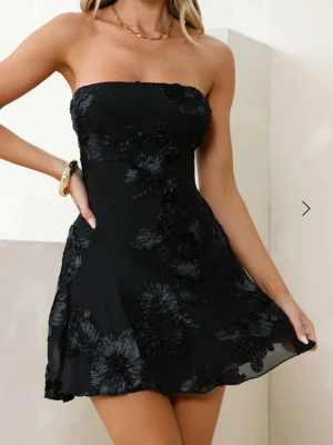 Strapless klänning  - Strapless svart klänning med blomdetaljer från Hello Molly. Använd en gång. 