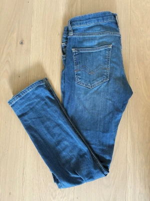 Replay Jeans 158 - Snygga blå skinny jeans från Replay med klassisk femficksdesign och diskreta slitningar. Jeansen har normal midja och smal passform hela vägen ner. Perfekta för en avslappnad och trendig look. Litet slitet märke på knät men annars bra skick