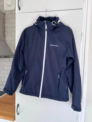 Vindjacka från Swedemount, storlek XS - Sportig och lätt vindjacka med 4-vägsstretch. Vind- och vattentät med tejpade sömmar, flera zip-fickor och avtagbar luva. Perfekt för både vardag och friluftsliv. Nypris: 999kr. * Material: 100% polyester. * Vattenpelare: 15 000 mm. (Fler bilder finns!)
