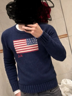 Mörkblå stickad tröja Polo Ralph Lauren - Mörkblå stickad tröja från Polo Ralph Lauren med amerikansk flagga i rött, vitt och blått på bröstet samt RL-broderi. Denna modell är lite mindre än de andra raffe tröjorna! Tröjan har rund hals, långa ärmar och ribbstickade muddar vid ärmslut och nederkant. Perfekt för en cool och avslappnad stil. || Det är bara o höra av sig vid minsta intresse! || priset är inte hugget i sten! ||