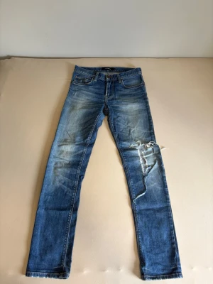J.Lindeberg slim fit jeans blå distressed - J.Lindeberg jeans i slim/skinny fit med snygg mellanblå wash och naturliga slitningar. Väldigt skön passform med stretch. Använda men fortfarande mycket liv kvar. Distressed look med slitning vid knät som ger jeansen extra karaktär. Perfekta för casual/streetwear outfit. Tvättas innan skickas  Storlek:  29/32