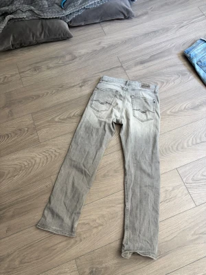 Grå raka jeans från Replay  - Säljer ett par grå jeans från Replay  med raka ben och klassisk femficksdesign. Jeansen har en snygg tvättad look och är tillverkade i bomullsdenim. Perfekta för en avslappnad och trendig stil.