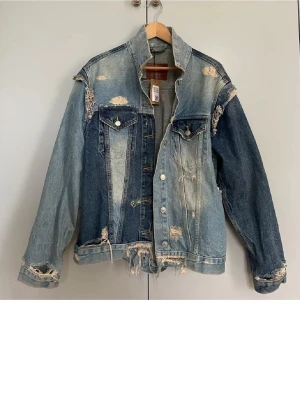 Oversized distressed jeansjacka - LÅNDADE BILDER! Säljer en oversized jeansjacka i olika blå nyanser med slitna detaljer och råa kanter. Jackan har två bröstfickor med knappar och en cool patchwork-design. Perfekt för dig som gillar en edgy och trendig stil. Kom privat för egna bilder!🩵💙