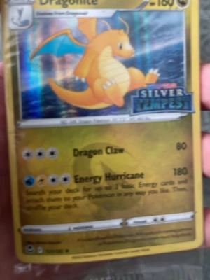 Pokémon promo kort Dragonite - Säljer ett Pokémon promo kort med Dragonite från Silver Tempest-serien. Kortet har en holografisk yta med motiv av Dragonite i orange och blått. Materialet är klassiskt papp/plast som används för samlarkort. Perfekt för Pokémon-entusiaster och samlare.