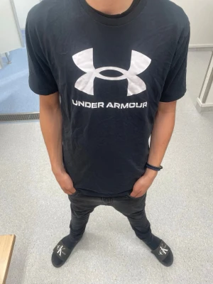 Svart Under Armour t-shirt - Svart t-shirt från Under Armour med stort vitt logotryck på bröstet. Klassisk passform med rund halsringning och korta ärmar. Perfekt för en sportig och avslappnad stil. M men passar som S