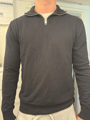 Svart halvzip-tröja Jack & Jones - Säljer en svart långärmad tröja från Jack & Jones med halvzip och hög krage. Tröjan är i mjukt material och har ribbade muddar vid ärmslut och nederkant. Perfekt för en clean och stilren look. Hör av er vid frågor!👍
