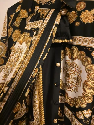 Svart och guldmönstrad skjorta och byxor  - Säljer en svart skjorta och byxor  med lyxigt barockinspirerat mönster i guld och vitt. Skjortan har långa ärmar, klassisk krage och knappar framtill. Materialet känns glansigt och mjukt, troligen polyester eller satin. Perfekt för dig som gillar statement-plagg.