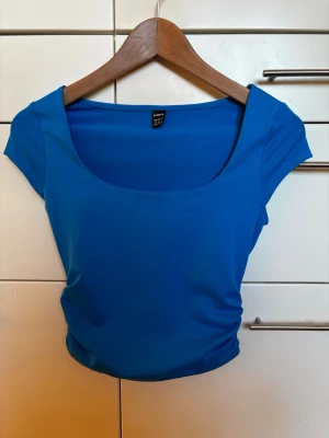 Blå tight topp med djup urringning storlek XS - Snygg blå topp från Shein med tight passform och korta ärmar. Toppen har en djup rundad urringning och är gjord i ett stretchigt, mjukt material. Perfekt skick! Storlek XS
