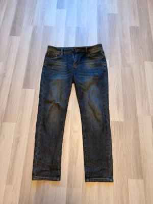 Mörkblå raka jeans från Ralph Lauren - Säljer ett par mörkblå jeans från Ralph Lauren med klassisk rak passform. Jeansen har fem fickor, bälteshällor och subtila slitningar framtill för en avslappnad look. Tillverkade i denim med snygga detaljer vid fickorna.