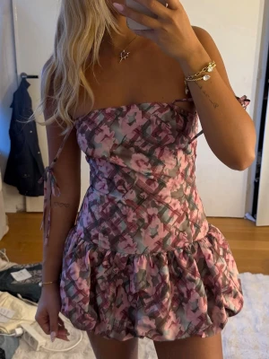 Blommig kort klänning med puffkjol - Supersöt kort klänning med puffig kjol och smala axelband. Klänningen har ett blommigt mönster i rosa, lila och gröna toner samt smock i ryggen för skön passform. 