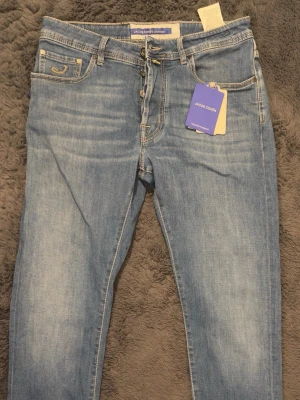 Ljusblå jeans från Jacob Cohën - Snygga ljusblå jeans från Jacob Cohën med klassisk femficksdesign och en tvätt man lätt kan justera bara man använder dom mycket. Jeansen har raka ben och normal midja, samt detaljerade sömmar och logotyp på bakfickan. Perfekta för en avslappnad och trendig look. Size 32. Använda en gång seriöst!