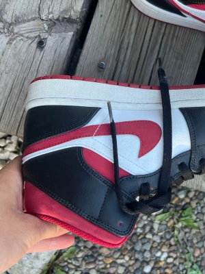 Air Jordan 1 Retro High OG röd/svart - Säljer ett par Air Jordan 1 Retro High OG med klassisk färgkombination i rött, svart och vitt. Skorna har svart läder, vita paneler och röda detaljer som swoosh och krage. Ikonisk Jordan Wings-logga på sidan och svart snörning. Perfekta för dig som gillar streetwear. Knappt använt dom finns kvitto, köpte de för 2100kr säljer de för 600 nu köpte de för 3 år sen 2023.