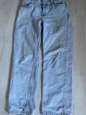 Ljusblå baggy/raka jeans i denim - Säljer ett par ljusblå jeans med rak/baggy passform och klassisk femficksdesign. Jeansen är tillverkade i denim och har en hög midja. Perfekta för en avslappnad och trendig stil.