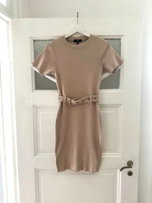 Beige kort klänning med bälte - Beige klänning med bälte i midjan. Storlek 34 men passar även 36. Stretchig och skön.