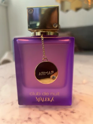 Club de Nuit Maleka parfym lila Armaf - Club De Nuit Maleka från Armaf är en Blommig fruktig doft för kvinnor. Detta är en ny doft. Club De Nuit Maleka lanserades 2025. Parfymören bakom denna doft är Olivier Cresp. Toppnoterna är Litchi, Bergamott och Rosa peppar; hjärtnoten är Irisrot; basnoterna är Praliner, Ambroxan och Sandelträ.Club de Nuit Maleka från Armaf är en parfym i en snygg lila, frostad glasflaska med silverdetaljer och en metallbricka som hänger i kedja. Flaskan rymmer 105 ml .