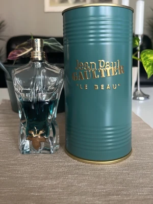 Jean Paul Gaultier Le Beau EdT 75ml - Jean Paul Gaultier Le Beau Eau de Toilette i en unik flaska formad som en manlig torso med blågrön vätska och gulddetaljer. Kommer med en stilren turkos metalltub med guldfärgad text. Perfekt för dig som gillar exklusiva och snygga parfymer.