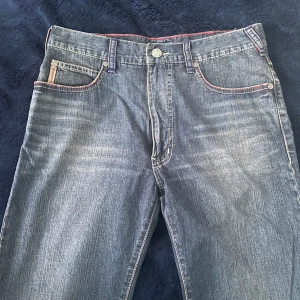 Blå jeans från Armani Jeans - Snygga blå jeans från Armani Jeans med klassisk femficksdesign och kontrastsömmar. Jeansen har en knappgylf och en läderpatch med logotyp på baksidan. Perfekta för en avslappnad stil. Helt ny,  Det enda oanvända paret som fortfarande håller formen och är i riktigt fint skick.
