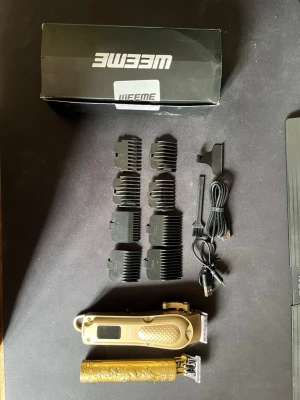 WEEME hårtrimmer guld, oanvända  - Säljer ett komplett hårtrimmer set från WEEME i guld med snyggt mönstrad detalj och drakmotiv. Paketet innehåller två trimmers, flera kammar, laddkabel och rengöringsborste. Perfekt för att fixa frisyren hemma.
