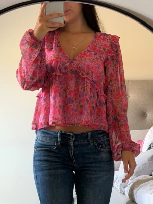 Blommig rosa blus  - Säljer en söt blommig blus i rosa och lila toner med volangdetaljer och v-ringning. Köpt på bik bok och är världens finaste sommartröja 💕