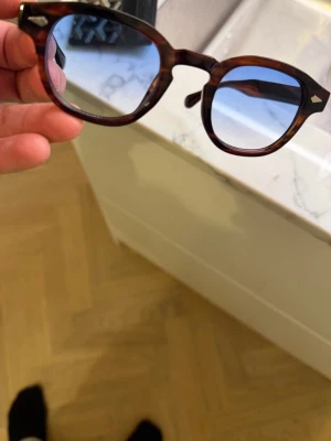 Oldmoney solglasögon med blått glas - Snygga solglasögon med rundad form och brunmelerat skal. Bågarna har en klassisk retrolook och är tillverkade i plast med coola detaljer vid gångjärnen. Perfekta för dig som vill sticka ut med en unik accessoar.