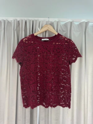 Vinröd spetsblus med kort ärm - Vinröd blus i spets med korta ärmar och rund halsringning. Blusen har ett genombrutet mönster och är perfekt för dig som vill ha en trendig och feminin look. Snygg att styla lager på lager eller som den är.