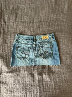 Ljusblå jeanskjol från Esprit - Snygg ljusblå jeanskjol från Esprit med fransig kant nertill och låg midja. Kjolen har detaljerade sömmar perfekt för sommaren.