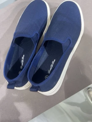 Mörkblå slip-on sneakers - Snygga mörkblå slip-on sneakers från Daniel De Paris med vit sula. Skorna har en enkel och stilren design i textilmaterial och elastiska paneler på sidorna för enkel påtagning. Perfekta för en avslappnad och trendig look.Perfekt för studenten och balen 