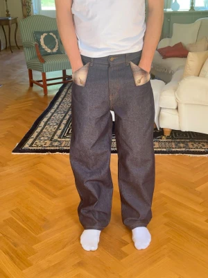 Mörkblå raw denim jeans, straight fit (bär en storlek större i bilden) - Säljer ett par mörkblå jeans i relaxed/straight fit. Jeansen har unika snedställda fickor med kontrasterande tygdetaljer. Klassisk femficksdesign och tillverkade i kraftig denim. Perfekta för dig som vill sticka ut med din stil. 13oz 