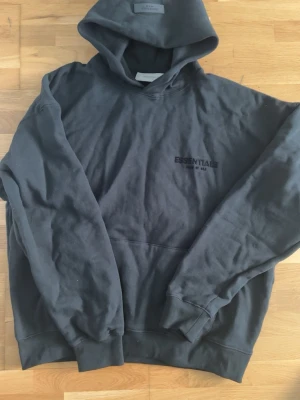 Svart Essentials Fear of God hoodie - Svart hoodie från Essentials Fear of God med tryck på bröstet och ryggen. Klassisk passform med huva och känguruficka. Tillverkad i mjuk bomullsblandning, perfekt för en avslappnad streetwear-look.