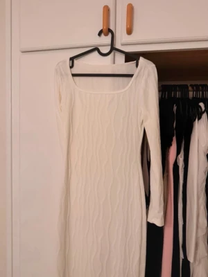 Vit långärmad ribbad klänning - Snygg vit långärmad klänning med ribbat vågmönster och fyrkantig ringning. Klänningen är kroppsnära och har en stilren look som passar perfekt till många tillfällen. Materialet känns mjukt och följsamt.Lite off white färg men sitter fint! den är även tyvärr lite genomskinlig och därför säljes den 
