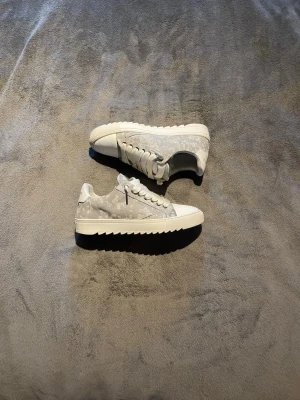  Numeris skor - Snygga sneakers från Numeris i grått och vitt med diskret mönster på ovandelen. Skorna har vita snören, räfflad sula och detaljer i mocka. Medföljer extra rosa skosnören och dustbag. Perfekta för dig som gillar stilrena och moderna sneakers.