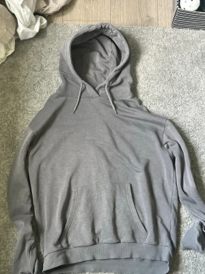Grå hoodie från RYVLS med huva - Säljer en enkel och stilren grå hoodie från RYVLS. Hoodien har en stor känguruficka framtill, dragsko i huvan och ribbade muddar vid ärmslut och nederkant. Mjuk insida för extra komfort, perfekt till chill dagar.