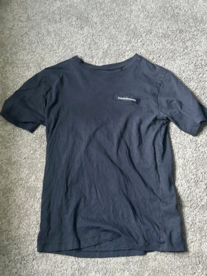 Mörkblå t-shirt från Peak Performance - En stilren mörkblå t-shirt från Peak Performance med liten logga på bröstet. Klassisk passform och rund halsringning. Perfekt till jeans eller shorts för en enkel och snygg look.
