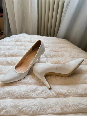Vita klassiska pumps med smal klack - Stilrena vita pumps med spetsig tå och smal klack. Skorna har en elegant siluett och är tillverkade i ett slätt material med matt finish. Insidan är ljusbeige och de har en tidlös design som passar till många olika looks. (Får med en skokartong på köpet)