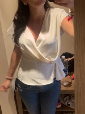 Vit omlottopp från Zara - Snygg vit omlottopp med korta ärmar och v-ringad hals. Toppen har en elegant omlottdesign som ger en fin siluett och passar perfekt till jeans eller kjol. Tillverkad i ett mjukt och följsamt material som känns bekvämt hela dagen.