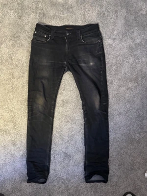 Svarta slim fit jeans från Nudie Jeans - Snygga svarta slim fit jeans från Nudie Jeans med klassisk femficksdesign och diskreta slitningar. Jeansen har en smal passform och är tillverkade i stretchigt denimtyg för extra komfort. Perfekta för en trendig och avslappnad look.