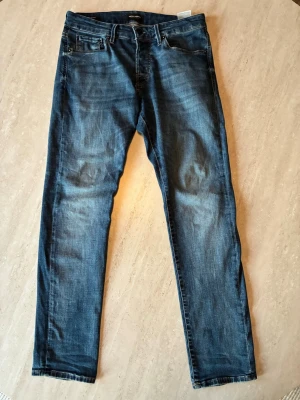 Blå slim fit jeans från Jack & Jones - Snygga blå slim fit jeans från Jack & Jones med klassisk femficksdesign och lätt slitna detaljer. Jeansen har normal midja och raka ben, perfekta till en avslappnad stil. Tillverkade i mjuk denim med stretch för extra komfort. Längd 31. Pris kan diskuteras 