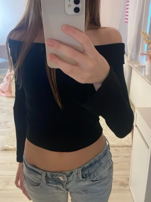 Svart offshoulder topp - Trendig svart offshoulder topp med lång ärm och croppad passform. Mjuk och stretchig kvalitet som sitter skönt på kroppen.